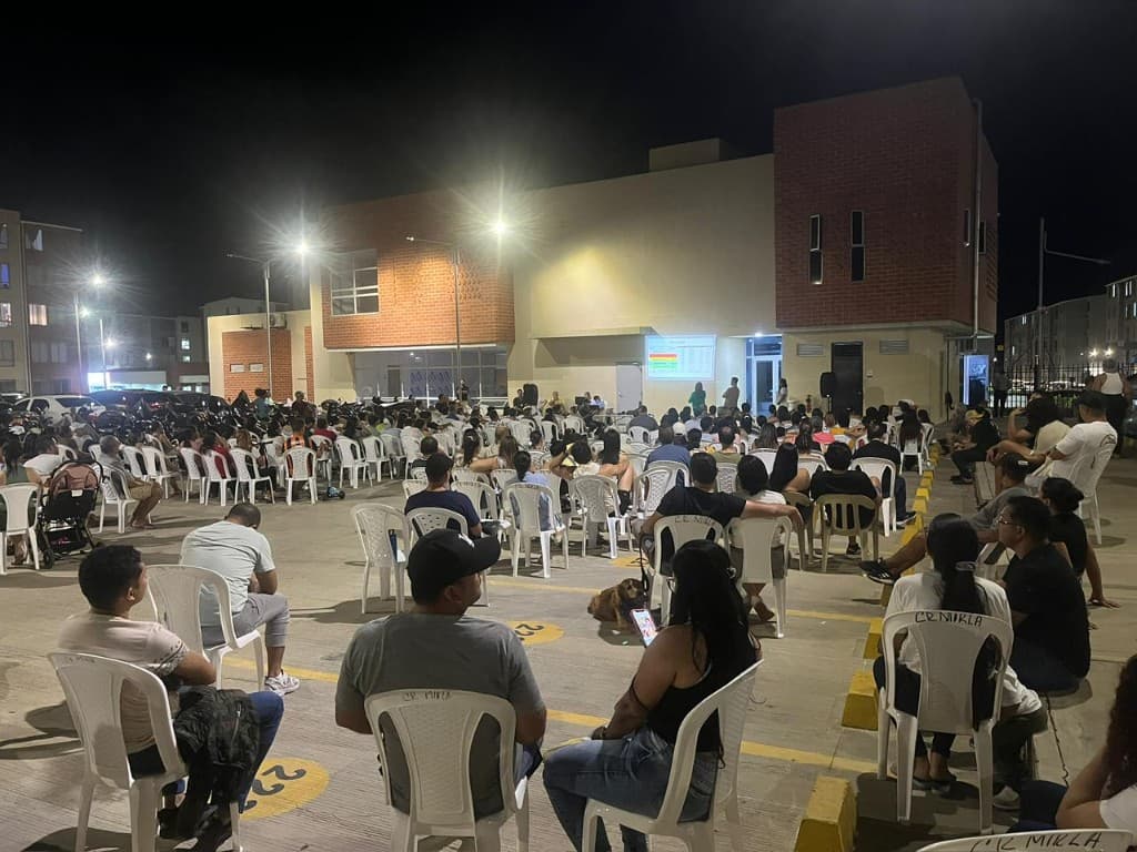 Asamblea nocturna con proyección en pantalla y copropietarios atentos